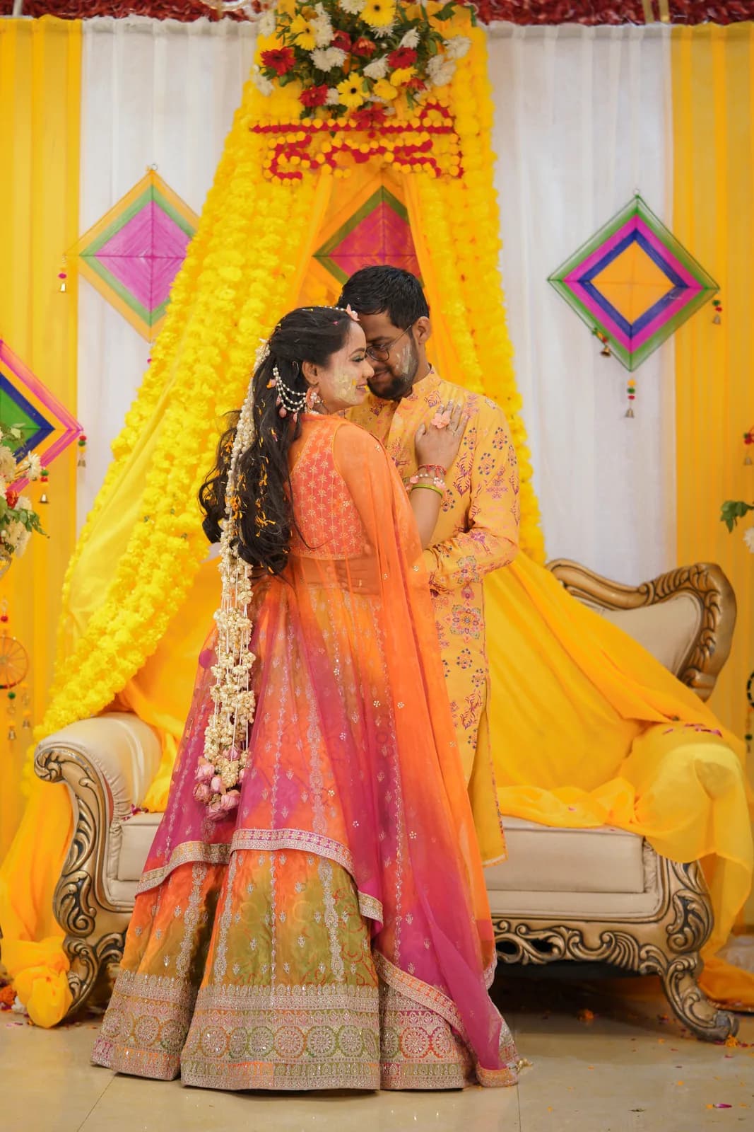 Bride laughing as female relatives apply yellow turmeric paste, hands and sari visible, natural window light